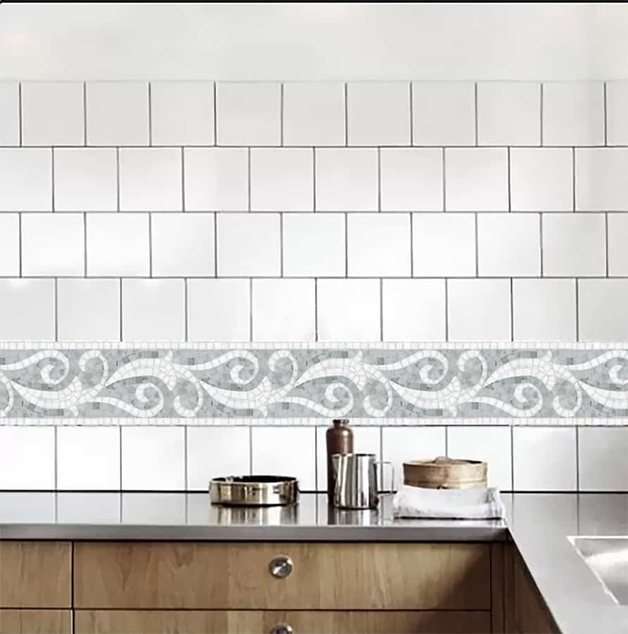 A custom hand-crafted grey and white MEC glass mosaic tile border featuring curling leaves and vines. 