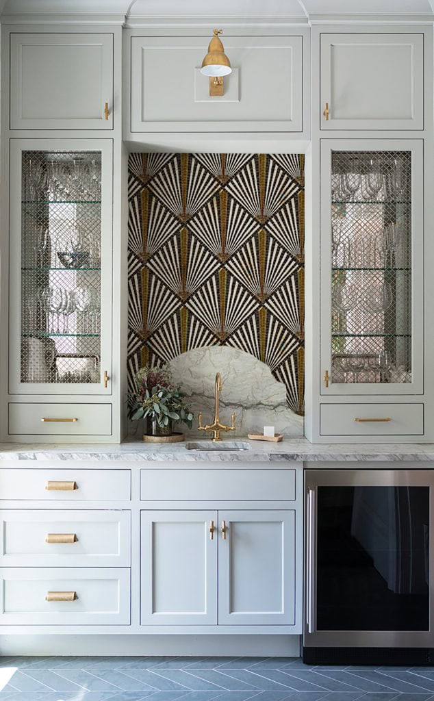 Modern kitchen with white cabinets, gold accents, and a backsplash featuring gold designs.